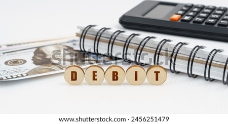 Business and finance concept. On a high surface lie a notepad, a calculator, dollars and wooden circles with the inscription - DEBIT