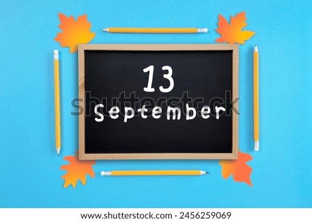 September 13 written in chalk on black board. Calendar date 13th of September on chalkboard on blue blurred school stationery background. Back to school. School event schedule date. Month of autumn.