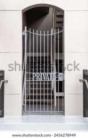 The exterior cream colored wall of a residence with a wrought iron gate at the entrance to the stairway. On the ornate metal gate the word private is forged. The sign restricts access to the property.