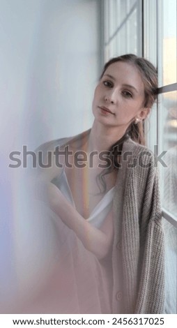 Beautiful young girl posing for the camera while sitting near a large window