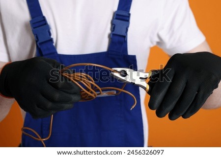 Young man holding pliers and wires on orange background, closeup