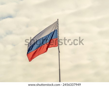 Russian tricolor flag waving in the wind against a blue sky. Russian flag on blue background