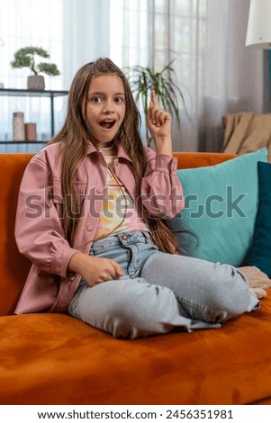 Eureka. Inspired girl pointing finger up having good idea, plan, startup, showing inspiration motivation gesture, problem solution. Young stylish child kid sitting on sofa couch in living room at home