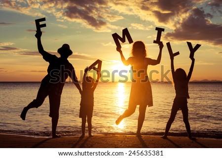 Happy family standing on the beach at the sunset time. They keep the letters forming the word " family". Concept of friendly family.