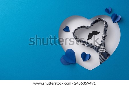 A creative arrangement featuring a heart-shaped cutout with a tie and mustache design, surrounded by smaller hearts in shades of blue, symbolizing Father's Day