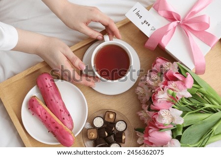 Tasty breakfast served in bed. Woman with tea, desserts, gift box, flowers and I Love You card at home, top view