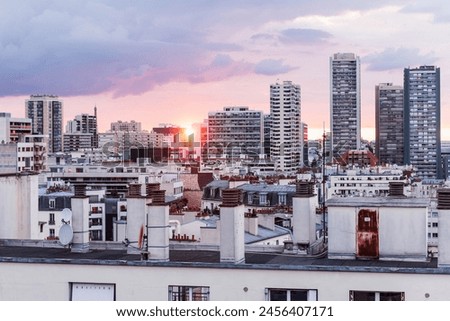 A breathtaking scene captures the sunset over Paris from the vantage point of a towering building, showcasing both grand and smaller buildings. The sun pierces through, casting a warm glow, illuminati