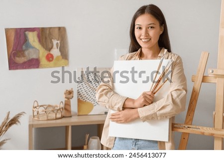 Female Asian artist with paint brushes and canvas at home