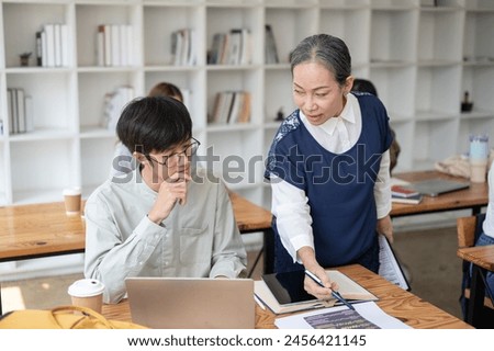 A mature Asian female teacher professor helping and explaining difficult math problems to her student in the class. education concept