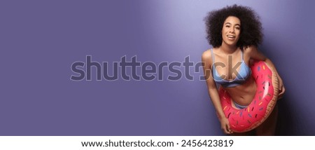 Beautiful African-American woman in bikini and with inflatable ring on purple background with space for text