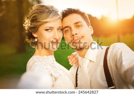 Young wedding couple taking a selfie of themselves as they enjoy romantic moments outside on a summer meadow