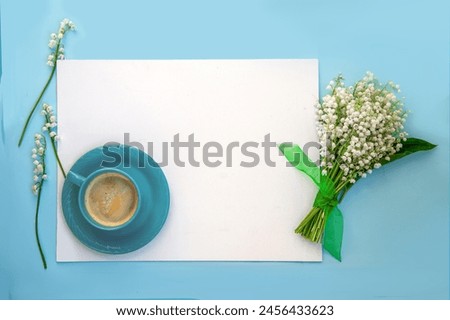 White sheet for text on a blue background with a cup of coffee and a bouquet of lilies of the valley