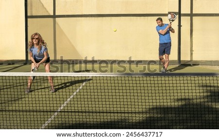 A mature man and woman enjoy a game of padel tennis outdoors during the golden hour, showcasing activity and fitness in later life. Royalty-Free Stock Photo #2456437717