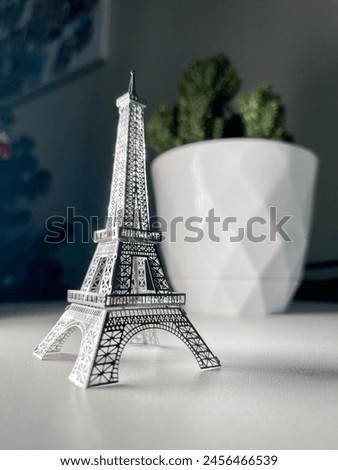 An isolated silver Eiffel Tower model on a white background with a blurred background of a cactus in a white pot.