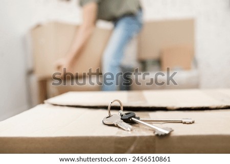 A close-up shot of house keys sitting on a box and a man yearning for the box in the background. Moving concept