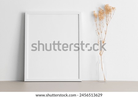 White frame mockup with a gypsophila decoration on the beige table.