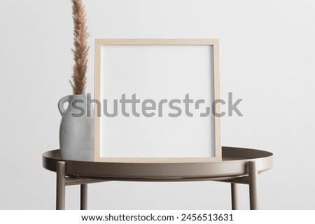 Wooden square frame mockup with a pampas decoration on the beige table.