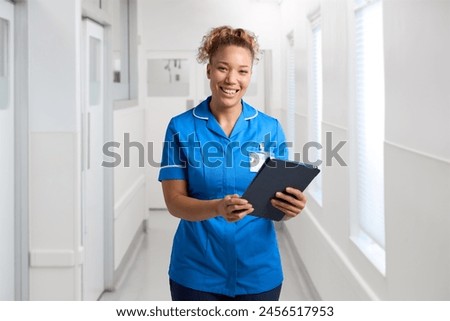 Portrait Of Smiling Female Nurse Wearing Uniform In Hospital Corridor With Digital Tablet
