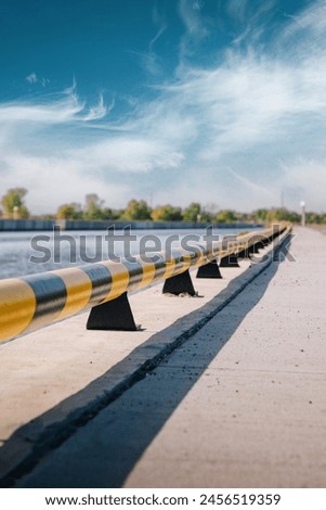 metal barrier in warning colours over concrete riverbank 
