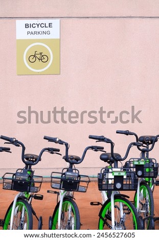 Row of bikes parked in bicycle parking area outside of building with parking sign label on stone beige wall background, front view and vertical frame