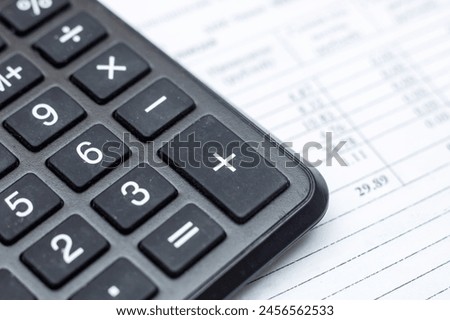 A closeup of a calculator, a peripheral input device, on top of a sheet of paper, office equipment often used with a computer keyboard or personal computer for calculations Royalty-Free Stock Photo #2456562533