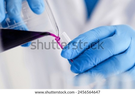 Male chemist holds test tube of glass in his hand overflows a liquid solution of potassium permanganate conducts an analysis reaction takes various versions of reagents using chemical manufacturing. Royalty-Free Stock Photo #2456564647