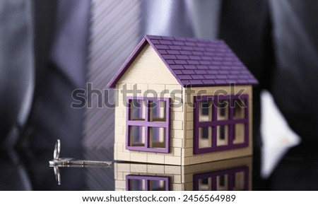 Man in suit and tie and silver key and little toy house at table closeup. New owner, pledge idea for life family solution male arm credit negotiation clerk in office future plan concept Royalty-Free Stock Photo #2456564989