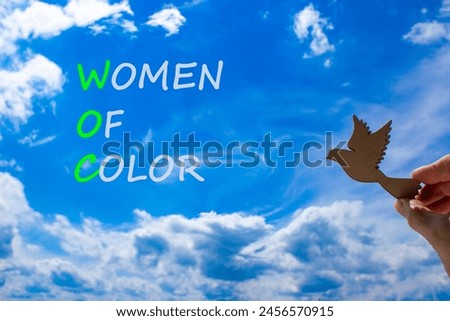 WOC women of color symbol. Concept words WOC women of color on beautiful blue sky clouds background. Wooden bird. Businessman hand. Business WOC women of color social issues concept. Copy space. Royalty-Free Stock Photo #2456570915