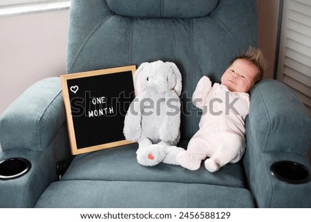 One month old Caucasian baby girl near the plush toy and letter board. Newborn baby monthly picture