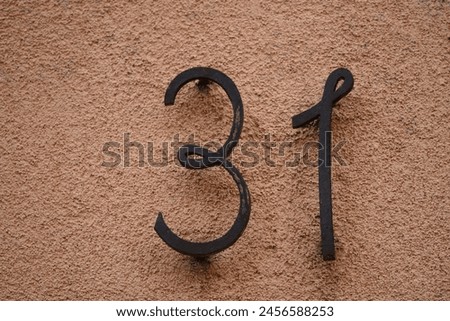 Antique cast iron street number sign against a textured wall in Bergheim, Alsace France. 