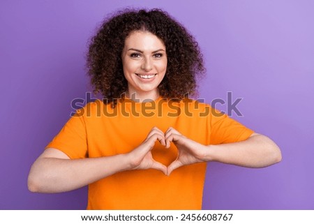 Photo of charming adorable lady dressed orange t-shirt showing arms heart gesture isolated violet color background