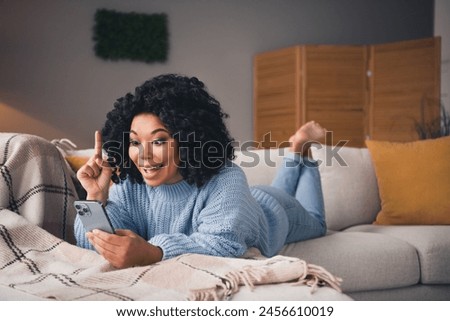 Full size photo of nice young woman lay sofa use phone point finger wear blue sweater modern interior apartment indoors