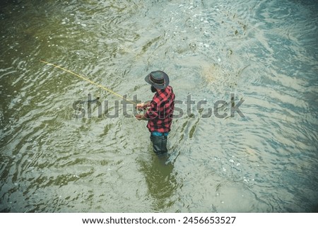 Young bearded man fishing at a lake or river. Flyfishing. Fisher man in water catching fish, top view. Royalty-Free Stock Photo #2456653527
