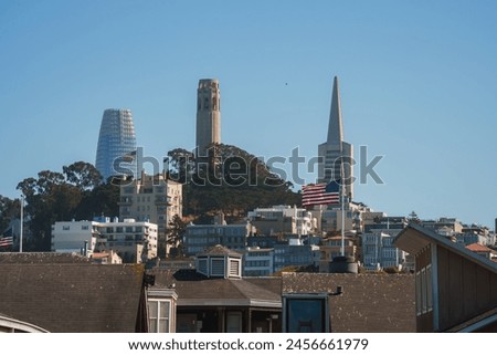 Scenic view of San Francisco showcasing architectural styles, residential buildings, hill with American flag, Coit Tower, Transamerica Pyramid, clear blue sky.