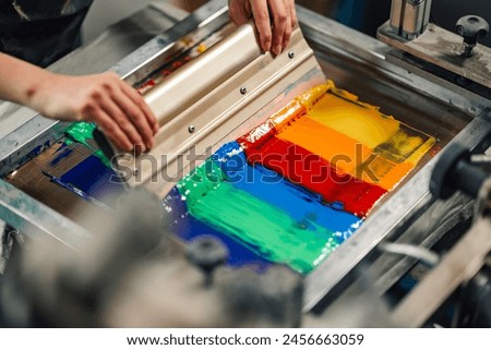 Close up of graphic technician's hands pressing ink into silk and screen printing with squeegee at printing shop. Cropped picture of print shop worker silkscreen printing with rubber blade in textile.