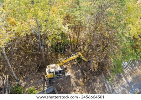 Making space for house by uprooting trees with an excavator tractor preparing site for construction Royalty-Free Stock Photo #2456664501