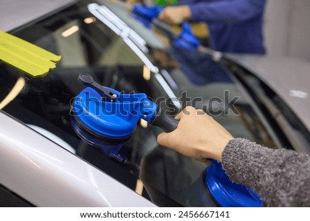 A person is installing a windshield on a car, along with automotive mirror, hood, and windscreen wiper, enhancing the vehicles automotive design and lighting