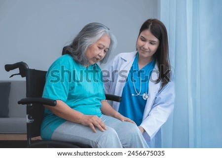 Asian woman doctor take care and encourage elderly patient Which sat on wheelchair, which she is saddened from depression, to elderly and health care concept Royalty-Free Stock Photo #2456675035