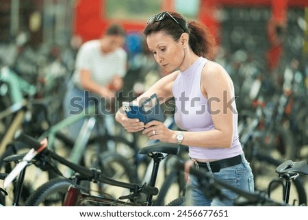 Adult woman buyer takes photo of bicycle on mobile phone in store