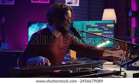 Skilled musician composing a song on piano midi controller, working with mixing console and daw software to record music. Artist singing at microphone, mastering his acoustical notes. Camera A.