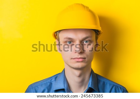 Young man close-up in yellow construction helmet and a blue shirt on a yellow background looking at the camera. Mimicry. Gesture. photo Shoot