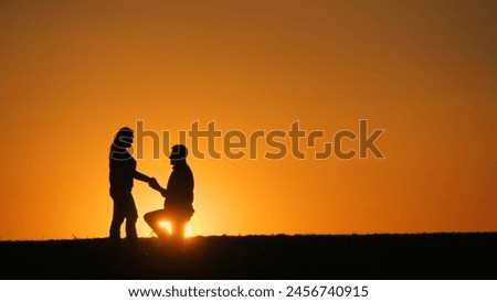 Silhouettes of a man and woman at sunset. A man is on one knee in front of a woman. Marriage proposal