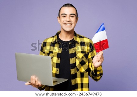 Young student IT middle eastern man wear yellow shirt casual clothes hold French flag use work on laptop pc computer isolated on plain pastel light purple background studio portrait. Lifestyle concept