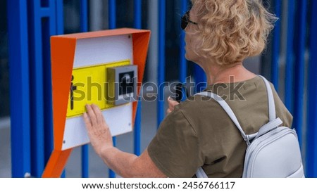 An elderly blind woman reading a text in braille. Button for calling help for people with disabilities. 