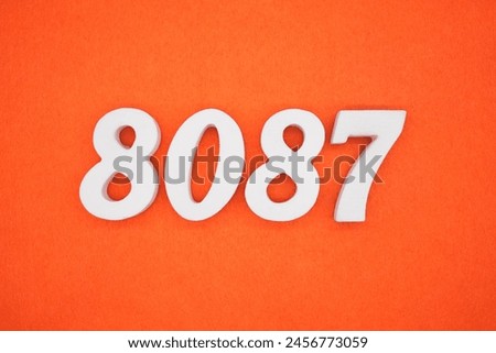 The number 8087 is made from white painted wood placed on a background of orange paper.