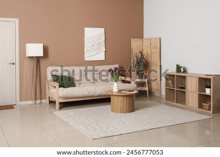 Interior of living room with cozy sofa, chest of drawers, coffee table and vase with tulips