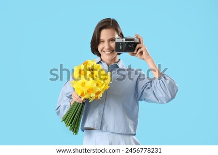 Young woman with daffodils and photo camera on blue background