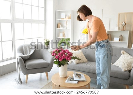 Young woman taking picture of pink roses in vase at home