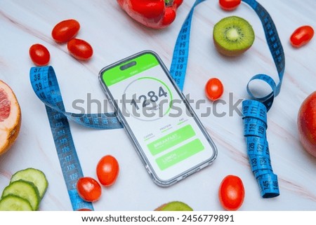 A calorie counting app displayed on a smartphone screen next to a tailor's measuring tape and a variety of healthy fruits and vegetables. Promoting mindful eating and nutrition tracking