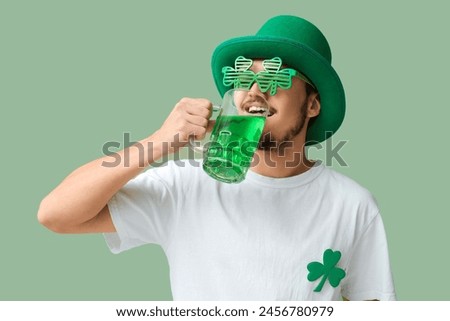 Handsome young man in leprechaun's hat with party glasses and mug of beer on green background. St. Patrick's Day celebration